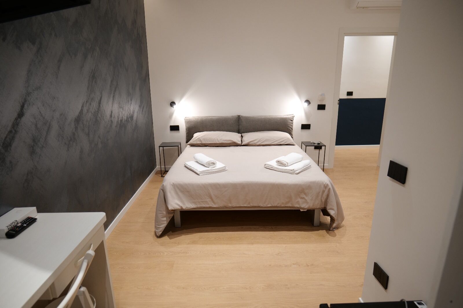 A modern hotel room with a large bed, bedside tables, and a desk with a chair.