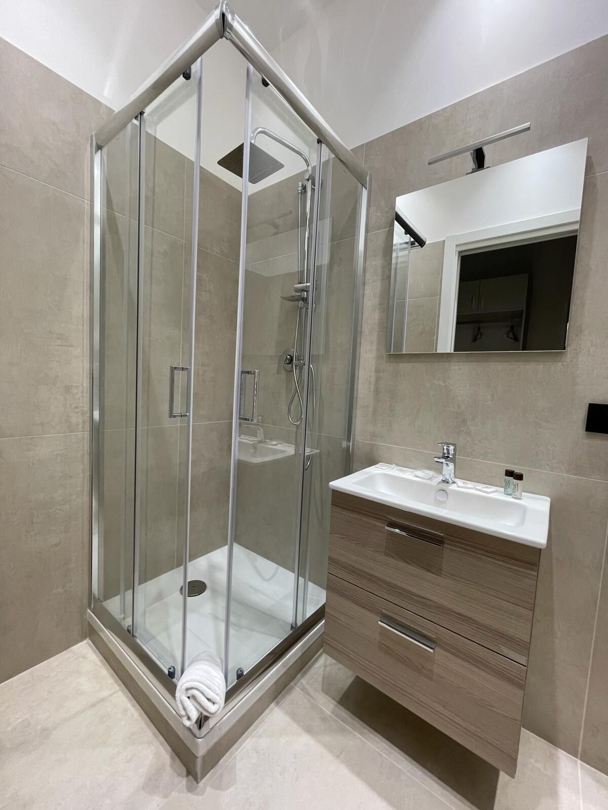 Un baño moderno con ducha de vidrio, tocador con lavamanos y espejo sobre el tocador.