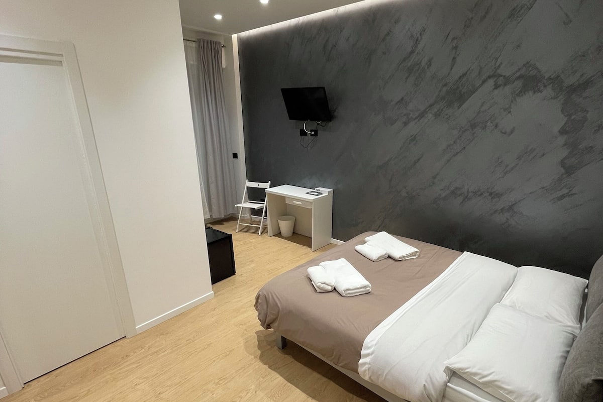 A modern hotel room with a bed, bedside table, and a TV mounted on the wall.
