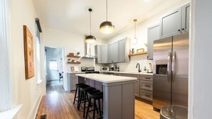 Une cuisine moderne dotée d’un îlot central, de tabourets de bar, d’appareils électroménagers en acier inoxydable et de luminaires suspendus.