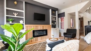 Un salon moderne doté d’une cheminée, d’un téléviseur à écran plat fixé au mur et d’un escalier menant à un autre niveau.