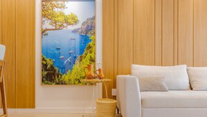 Un salón moderno con un sofá blanco, una pared de madera y un cuadro grande con un paisaje costero.