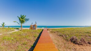 Un sendero de madera que conduce a una playa con palmeras y un cielo azul despejado.