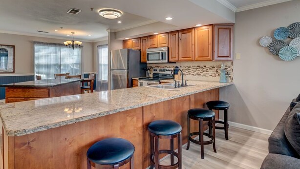 A spacious kitchen with wooden cabinets, a granite countertop, and a central island with bar stools. - Walk In luxury condo with pools and hot tub! Comfy beds! (Branson)
