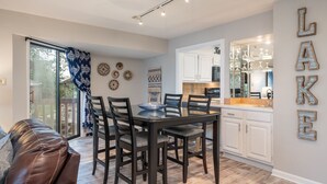 A modern kitchen with white cabinets, a glass backsplash, and a dining area with a dark wooden table and chairs.
