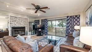 A modern living room with leather sofas, a glass coffee table, a fireplace, and a large TV.