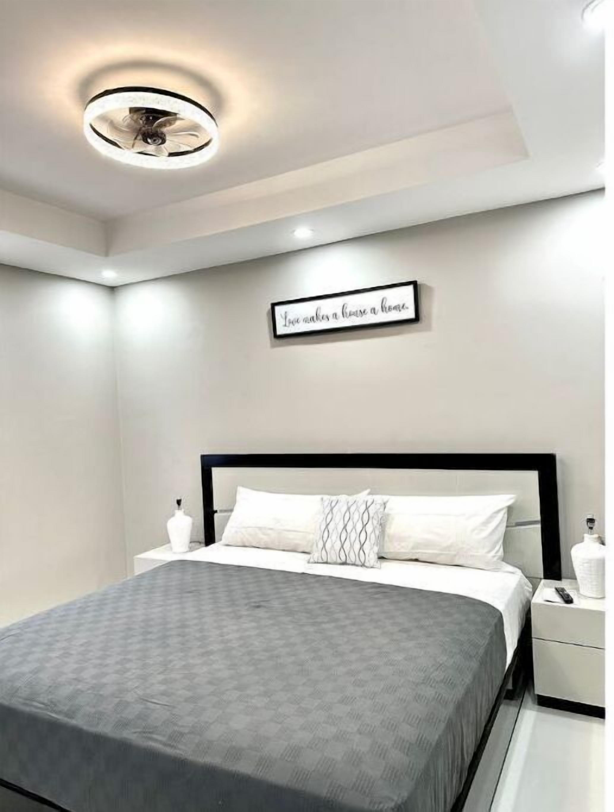 A modern bedroom with a bed, nightstands, a ceiling light, and a motivational quote on the wall.