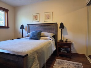 Un dormitorio con una cama, dos lámparas de noche, una mesita de noche, un tapete y dos cuadros en la pared.