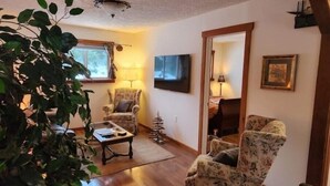 Un salón acogedor con piso de madera, un sillón floral, una pequeña mesa de centro y una lámpara.