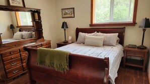 Un dormitorio con una cama de madera, un aparador, una mesita de noche, una ventana con persianas y un espejo.