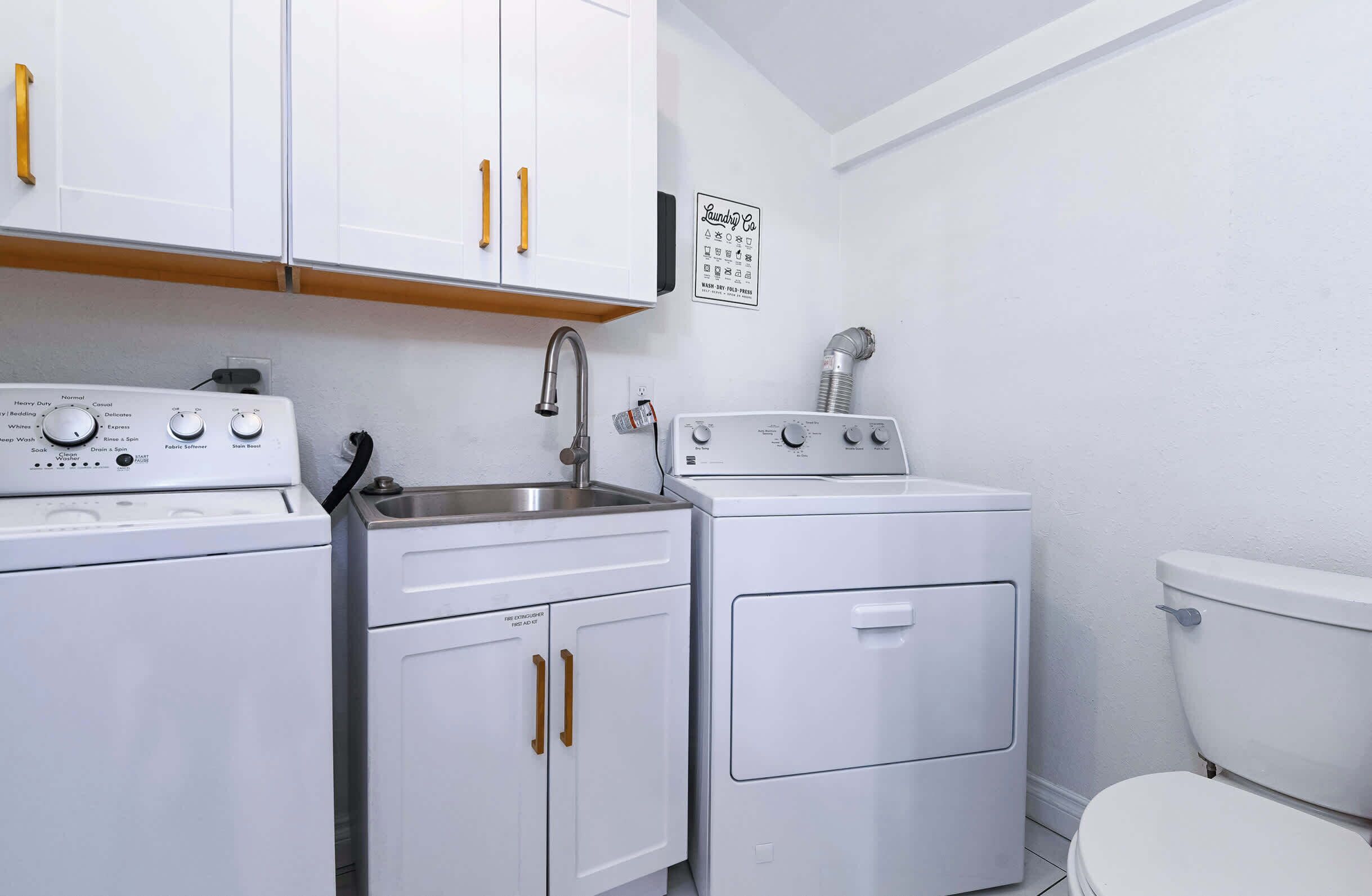 A compact kitchen with a washing machine, a dryer, a sink, and a toilet.