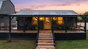 A log cabin with a wooden deck, a porch with chairs, and a metal roof. - The Hendo - Cabin #1 - Studio Style (Henderson)