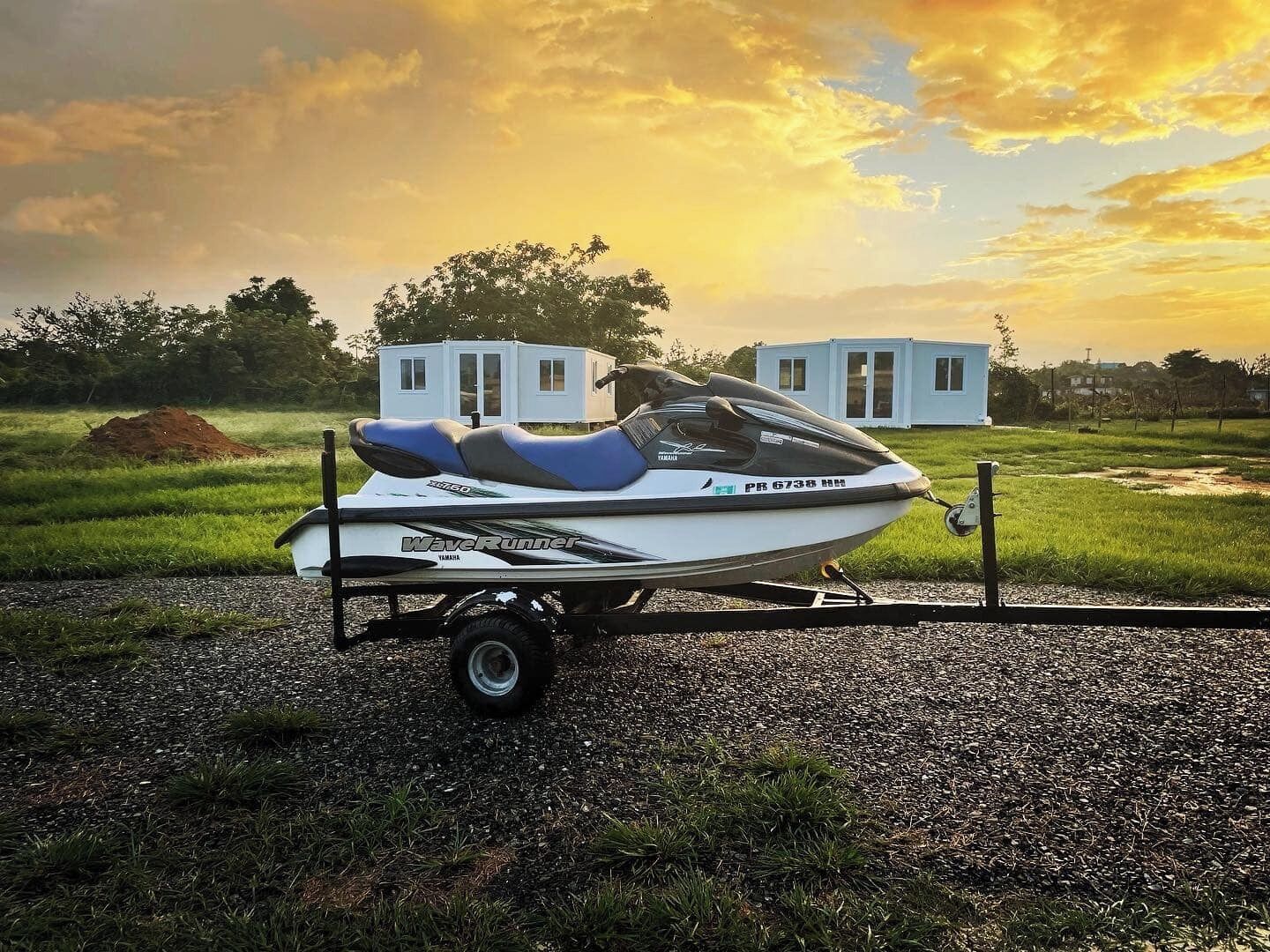 A Yamaha WaveRunner jet ski on a trailer in a grassy field with a small white building in the background.