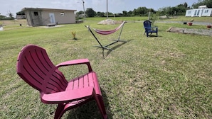 A grassy outdoor area with a hammock, a red chair, and a blue chair.