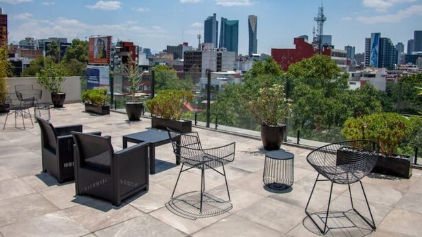 Eine Dachterrasse mit Sitzgelegenheiten im Freien, Topfpflanzen und Blick auf die Skyline der Stadt.