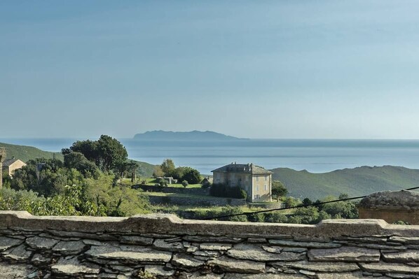 A stone wall with a view of a small, isolated house surrounded by greenery and hills.