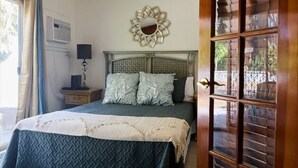 A bedroom with a bed, a nightstand, a wall-mounted mirror, and a window with blinds. - Located on Paradise Island, Bahamas, close to the Atlantis Resort and beach.  (Nassau)
