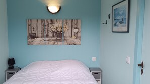 Un dormitorio con una cama, una mesita de noche, una lámpara, luz empotrada en la pared y un cuadro enmarcado.