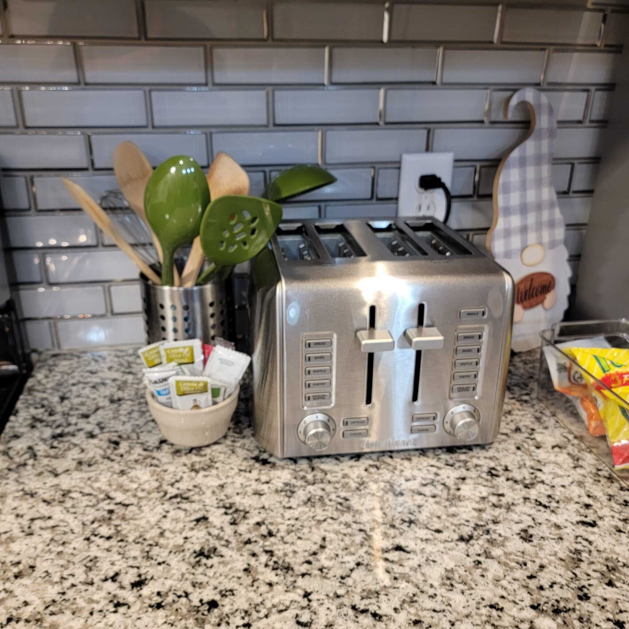 Eine Küche mit einem Edelstahltoaster auf einer Granit Arbeitsplatte, einer Schale mit Kaffeekapseln und einem dekorativen Willkommensschild.