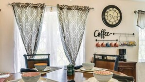 Een eetruimte met een ronde tafel, behang met patroon, een kroonluchter en een wanddecoratie met koffie thema.