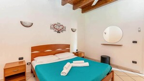 A bedroom with a wooden bed, a nightstand, a wall-mounted mirror, and a small trash bin.