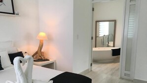 Una habitación de hotel con una cama, una lámpara, una decoración de toallas con forma de cisne y vistas a un baño con lavamanos y espejo.