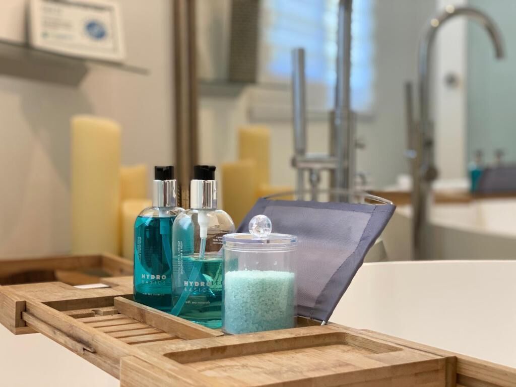 A wooden tray with a bottle of blue liquid, a glass jar with blue granules, and a small container on a bathroom counter.