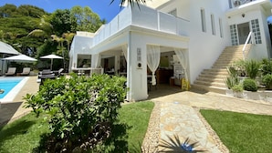 Una casa blanca de dos pisos con piscina, mobiliario exterior y una escalera que conduce al nivel superior.