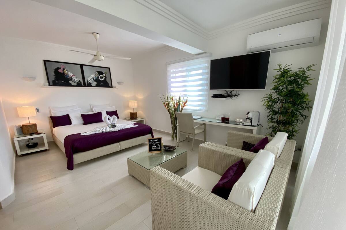 A modern hotel room with a bed, a sofa, a desk, and a TV.