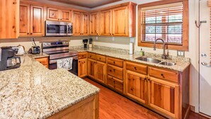 Una cocina con armarios de madera, encimeras de granito, electrodomésticos de acero inoxidable y una ventana con persianas.