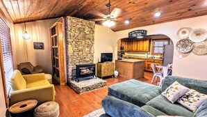 Una sala de estar acogedora con chimenea de piedra, techo de madera y una zona de cocina con armarios de madera.