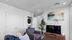 A modern living room with a sofa, a coffee table, a flat-screen TV, a washing machine, and a large painting on the wall. - Luxury Apartment in Salt Lake City (Salt Lake City)
