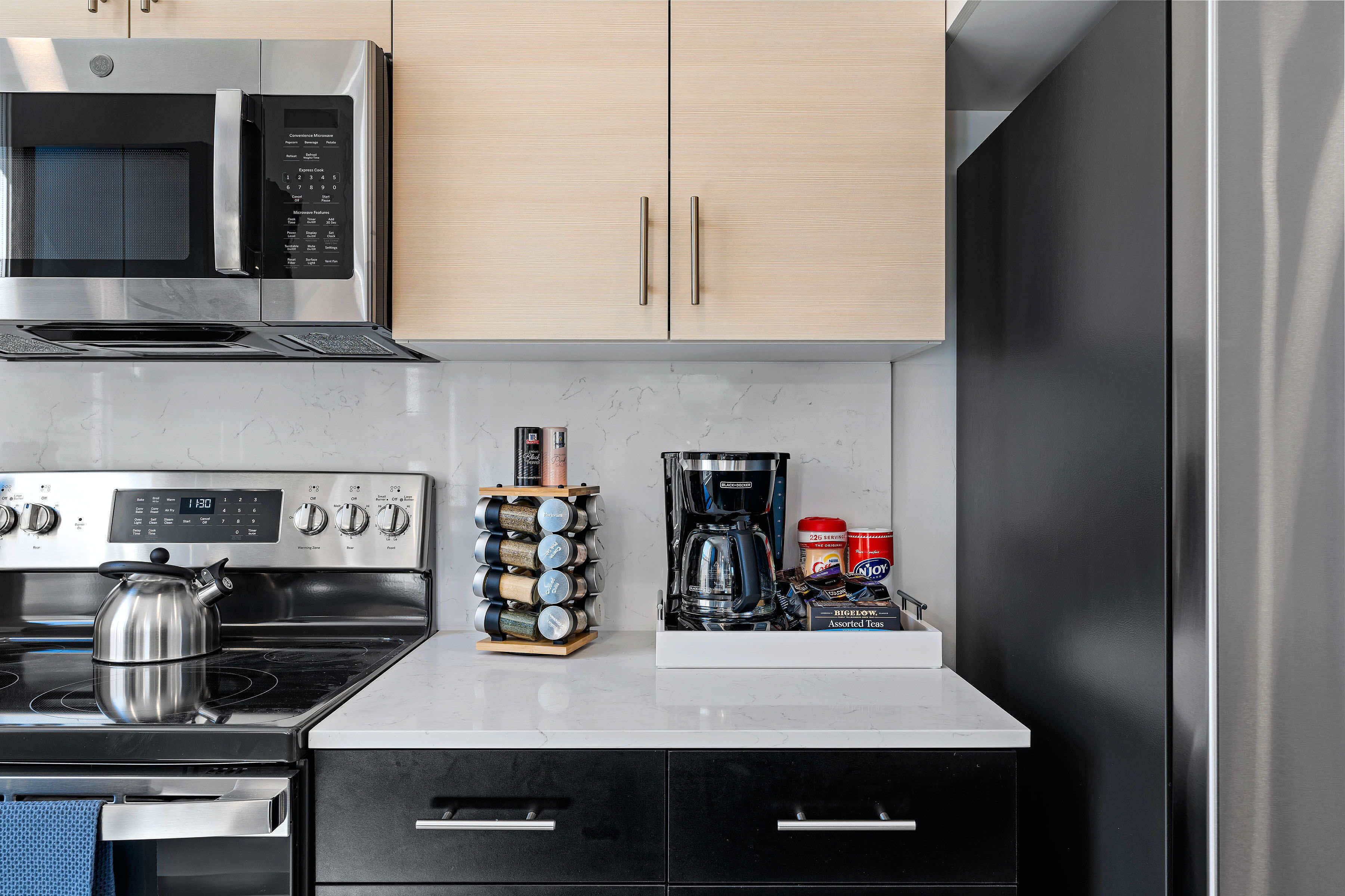 A kitchen with a microwave, stove, oven, and coffee maker. There are cabinets above the counter and a coffee machine on the counter.