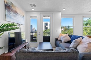 A modern living room with a flat-screen TV, a dark coffee table, and a grey sofa with multiple cushions. There is a large abstract painting on the wall and a potted plant to the left. - Luxury Apartment in Salt Lake City (Salt Lake City)