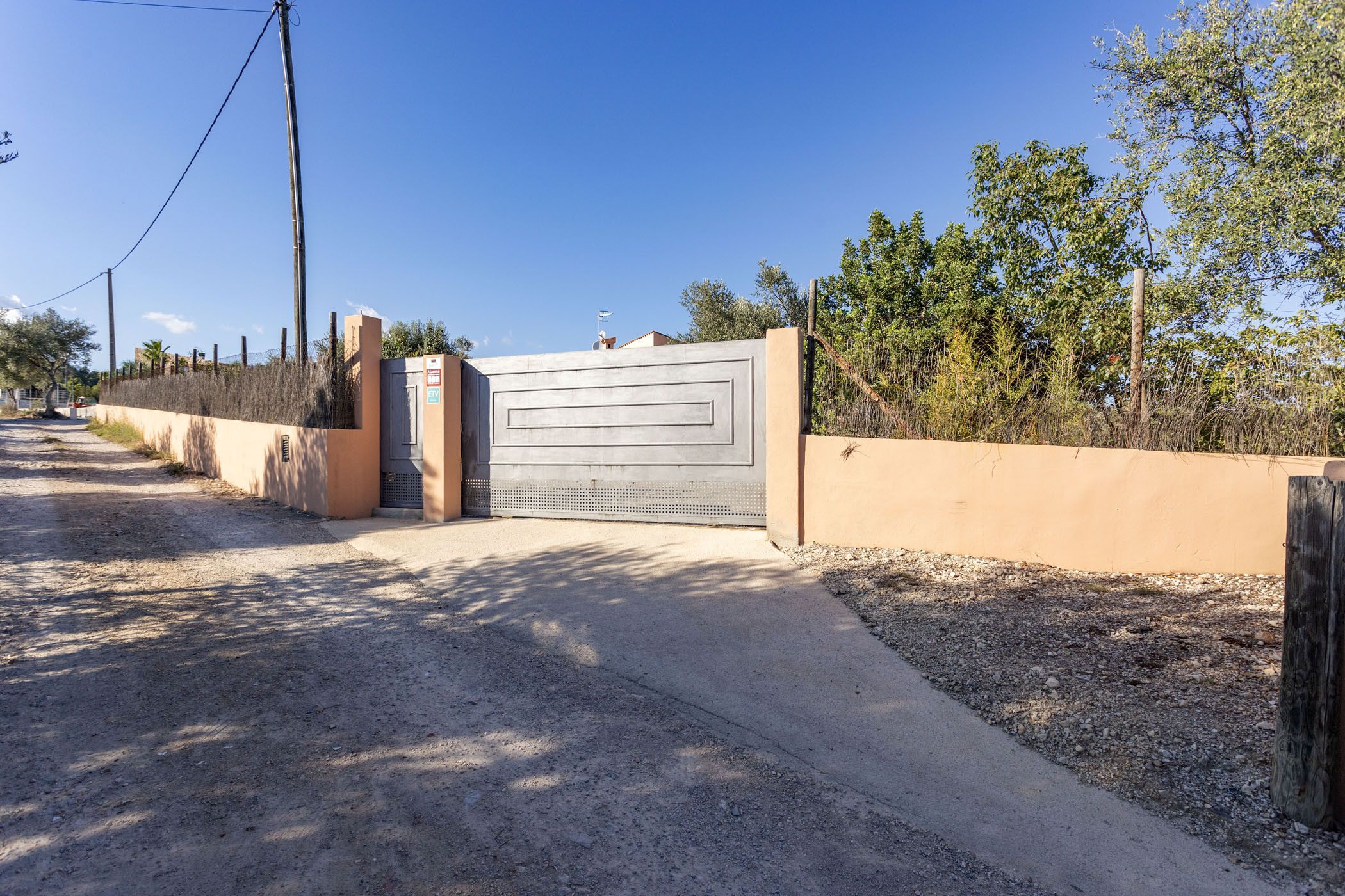 A gated entrance with a metal gate, a concrete wall, and a gravel path leading to a building.