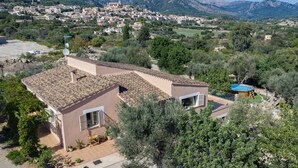 A residential area with a house featuring a tiled roof, a small garden, and a view of a town in the background.