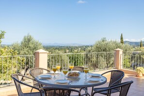 Une table ronde entourée de chaises, sur un balcon donnant sur un paysage pittoresque.