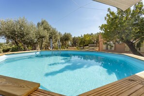 Une piscine d’un bleu éclatant, dotée d’une terrasse en bois, entourée d’arbres et bordée d’un bâtiment.