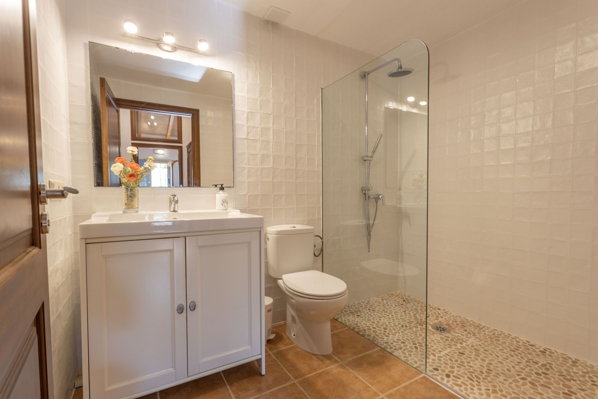 A bathroom with a glass shower enclosure, a white toilet, and a vanity with a mirror.