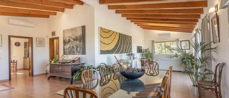 A spacious dining area with wooden beams, a glass table, and chairs.