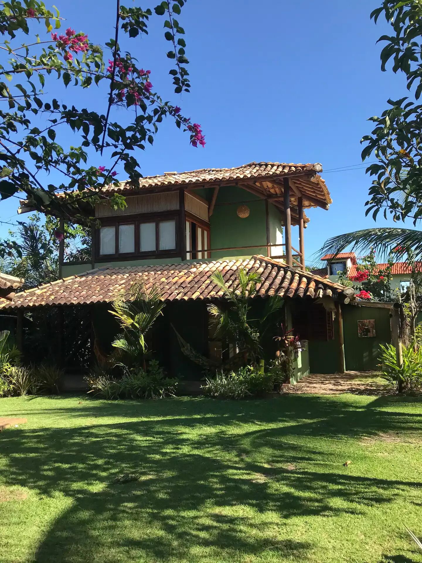 A two-story house with a tiled roof, surrounded by lush greenery and a well-maintained lawn.