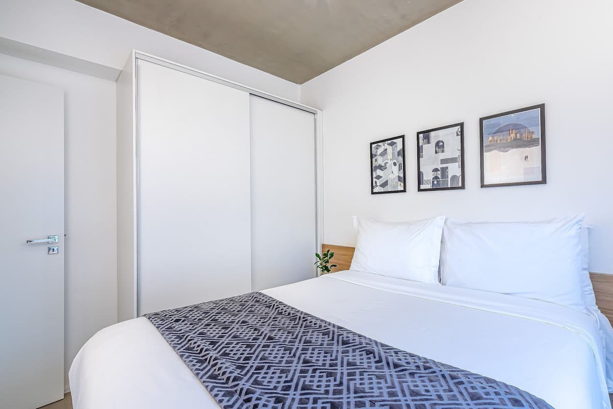 Un dormitori amb un llit, una porta blanca i dos quadres al mur.