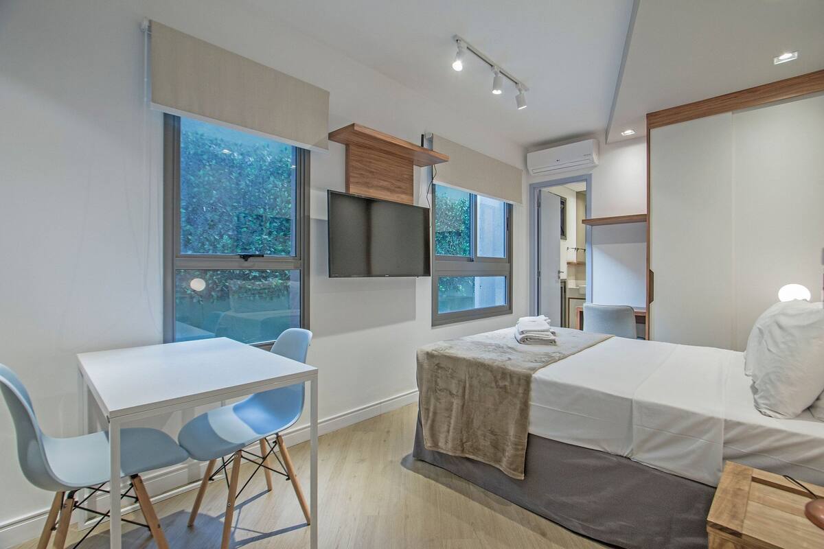 Habitació d'hotel moderna amb llit, escriptori, cadires, televisió i finestres grans.