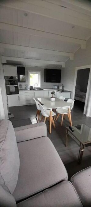 Een moderne woonkamer met een grijze bank, een glazen salontafel en een eethoek met een witte tafel en stoelen.