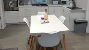 Et moderne køkken med hvide skabe, et spisebord med stole og en mikrobølgeovn.