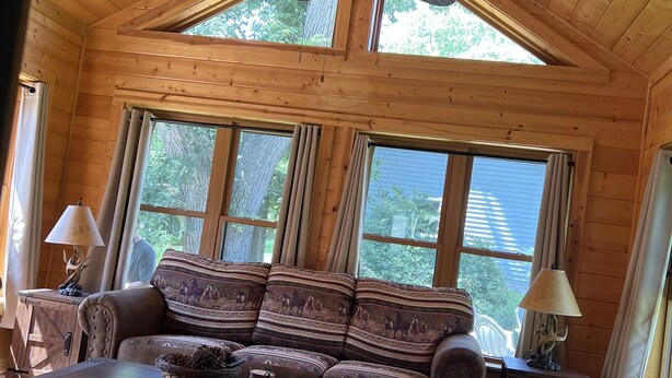 Ein gemütliches Cabin-Interieur mit Holzbalkendecke, Deckenventilator, Sofa mit gemusterten Kissen, Couchtisch und zwei Lampen auf Beistelltischen.