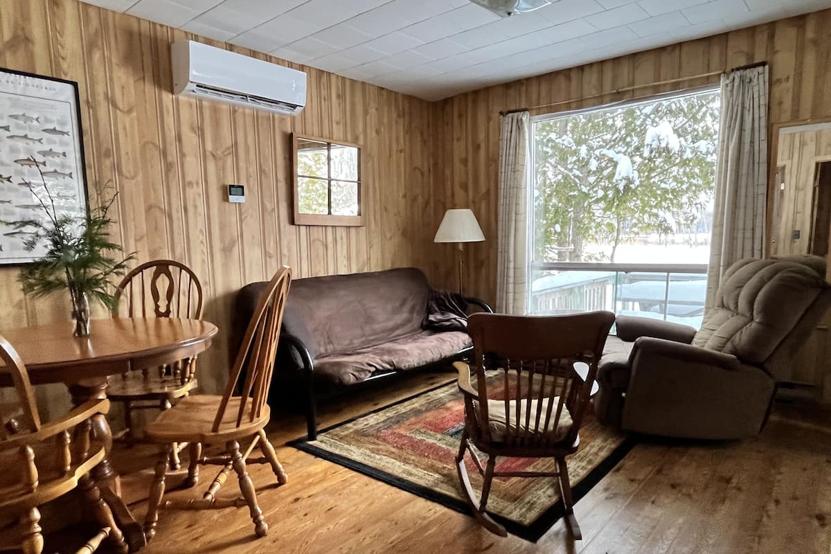 A wooden-paneled room with a dining table, chairs, a sofa, and a rocking chair.