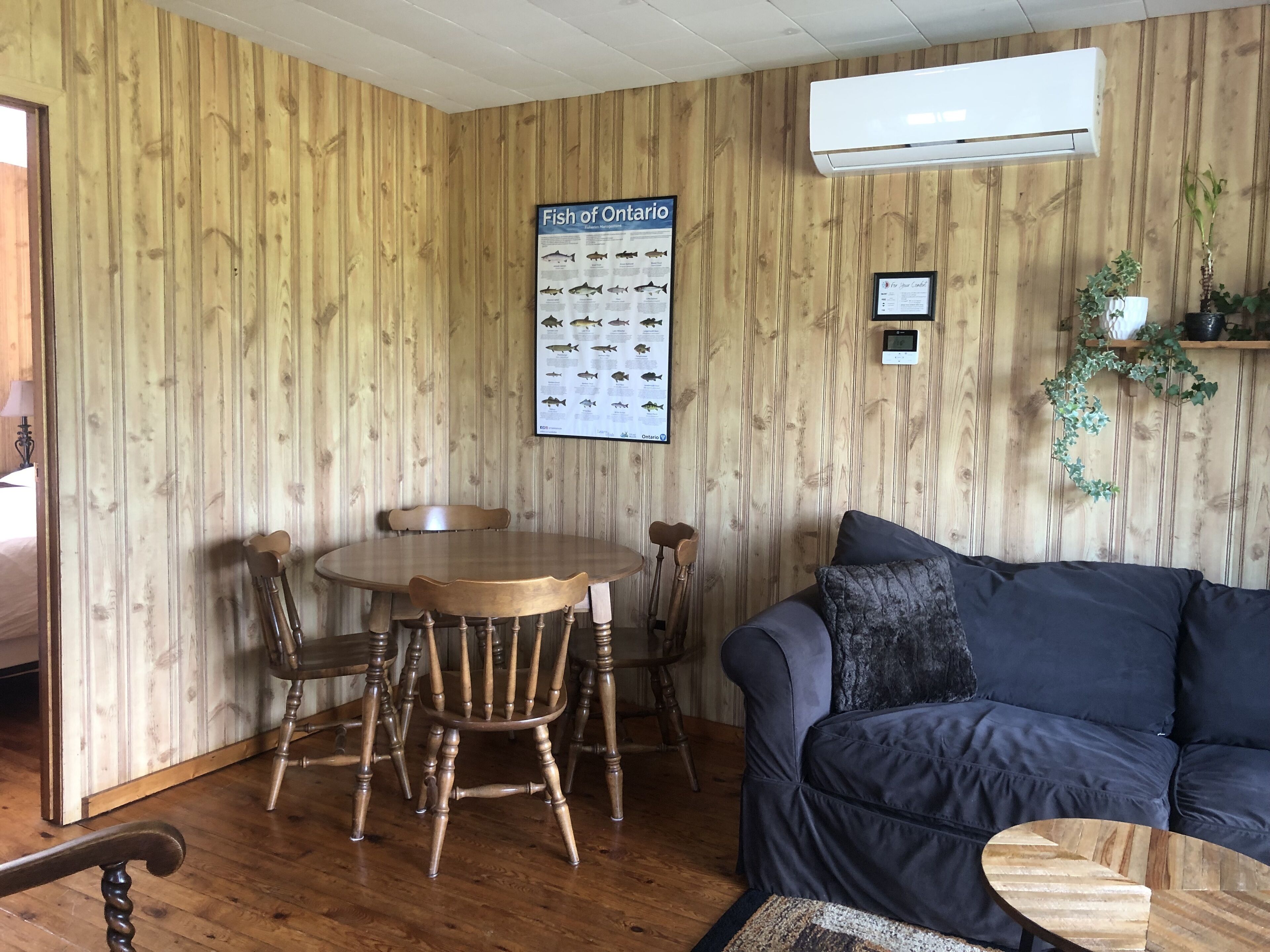 Una habitación con paneles de madera, una mesa redonda de madera y cuatro sillas, un sofá azul y una pequeña mesa de centro de madera.