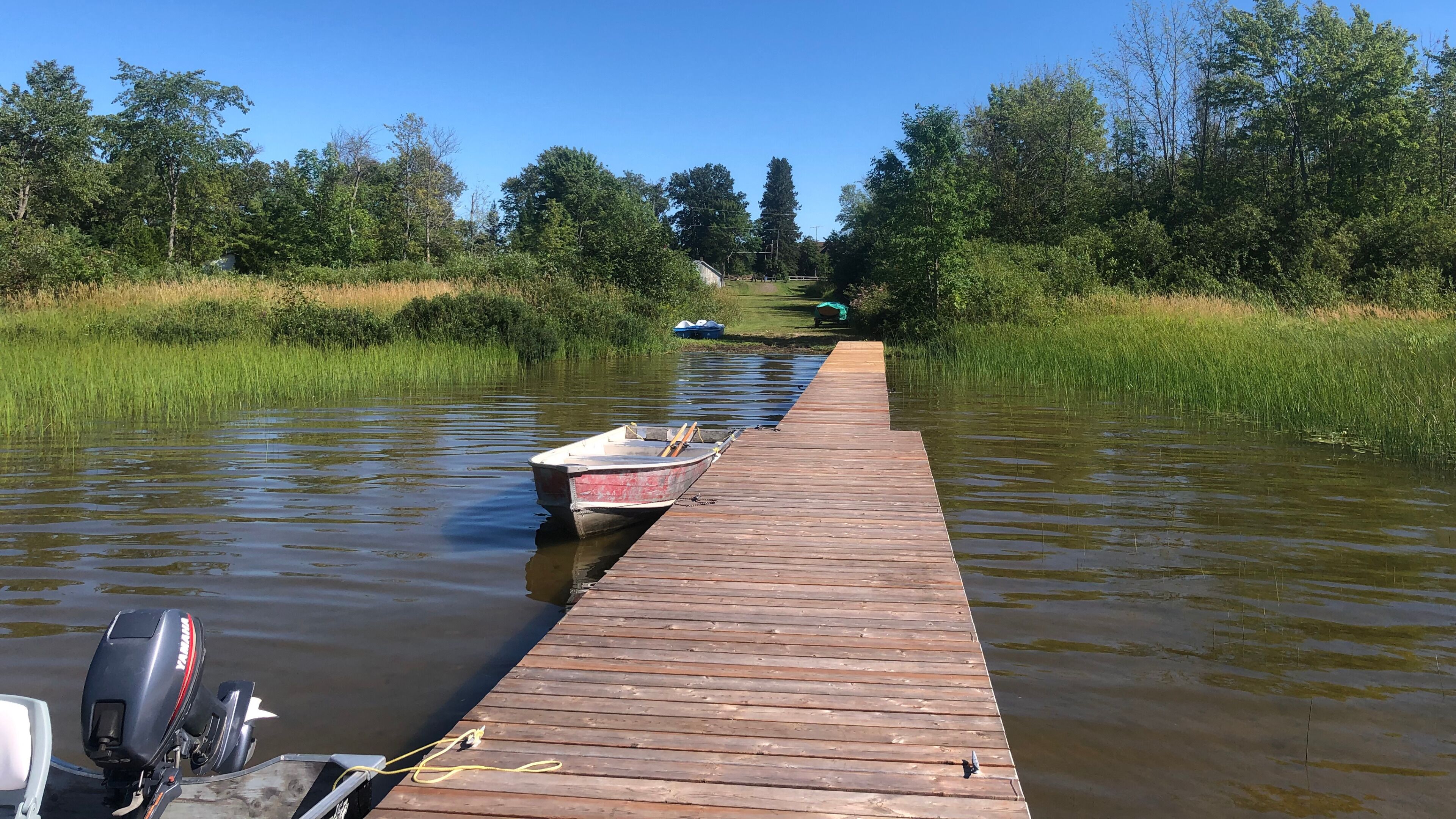 A wooden dock extending into a calm body of water with a boat moored at the end.