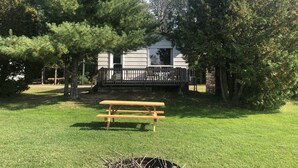 A cabin with a deck, surrounded by trees, and a picnic table in the foreground. - Staying by the Lakeside Cottages (Plummer Additional)